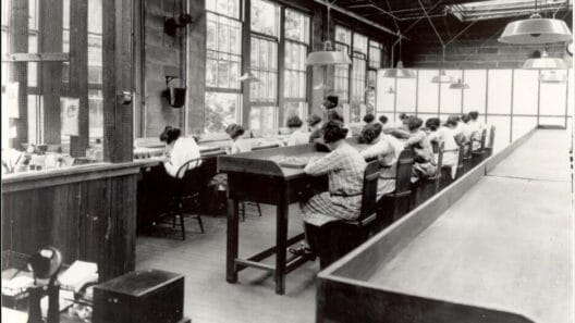 Radium Girls: la tragedia del radio que cambió la salud laboral 3 Fila de trabajadoras sentadas en una fábrica pintando manualmente esferas de reloj junto a grandes ventanales