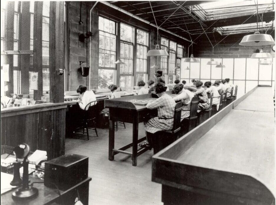 Radium Girls: la tragedia del radio que cambió la salud laboral 6 Fila de trabajadoras sentadas en una fábrica pintando manualmente esferas de reloj junto a grandes ventanales