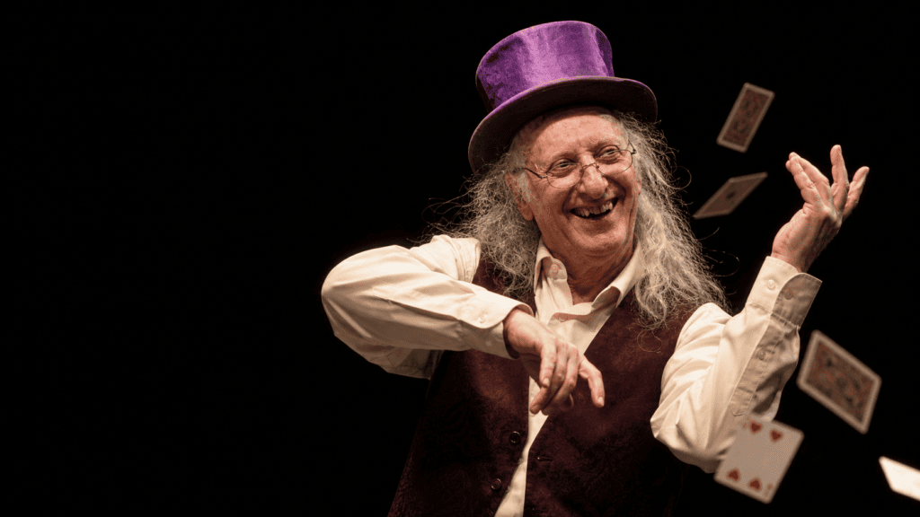 Recreación artística hiperrealista de Juan Tamariz con chistera morada y chaleco, sonriendo mientras toca su violín imaginario y hace levitar cartas