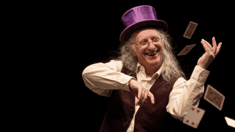 Recreación artística hiperrealista de Juan Tamariz con chistera morada y chaleco, sonriendo mientras toca su violín imaginario y hace levitar cartas